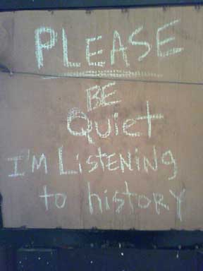 detail photograph of Zach Cahill's sculpture installation Pink City (2007), a cardboard sign that reads Please be quiet I'm listening to history