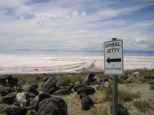 photograph of Robert Smithson's Spiral Jetty earthworks sculpture, a rock and dirt spiral that curls into the north end of the Great Salt Lake; a sign next to it reads, 'Spiral Jetty, End of Road' 